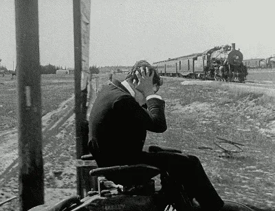 Black-and-white photograph of a man seated near a railway track as a train approaches